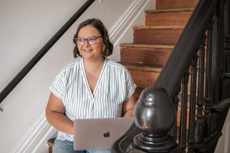 website designer sitting on a staircase with a laptop smiling
